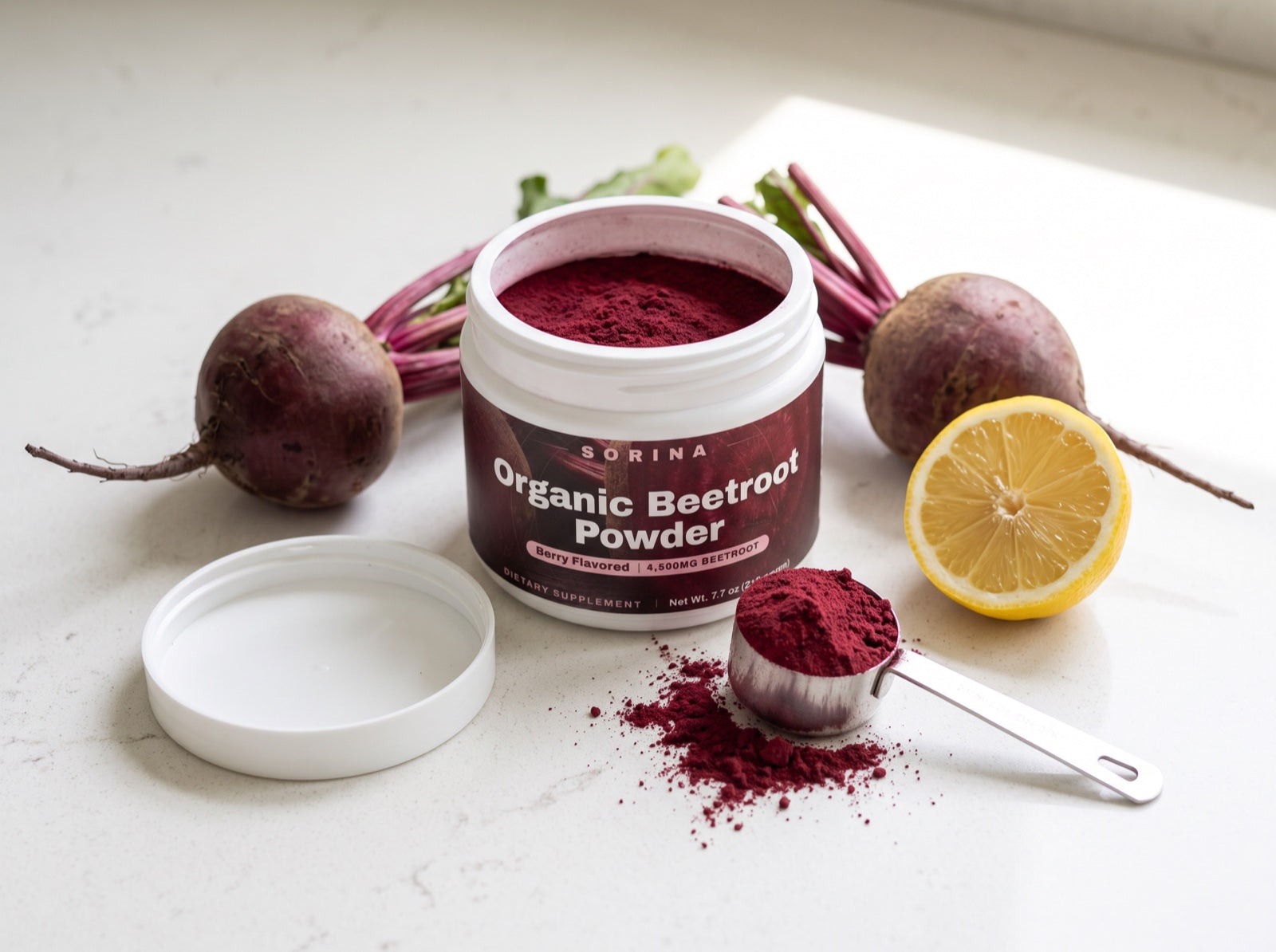 Overhead of the open beetroot tub with a scoop of red powder, fresh beets and a halved lemon on a light counter
